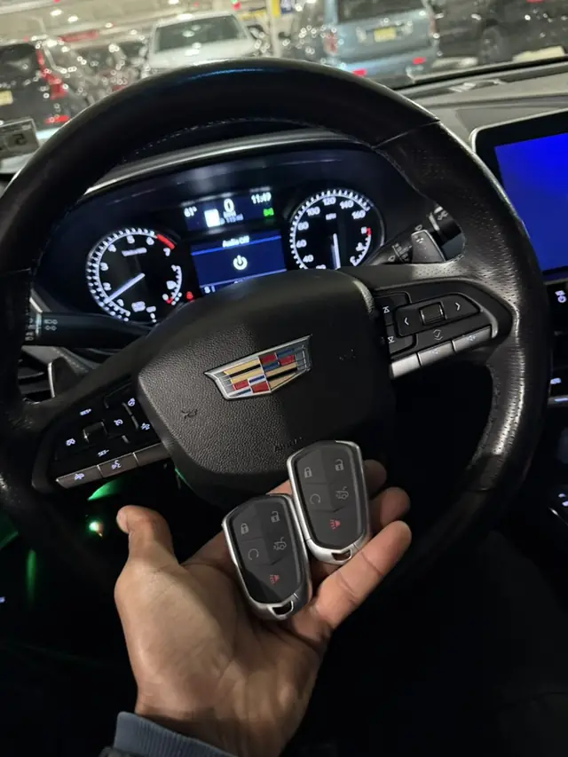 Two Cadillac smart keys held in front of a Cadillac steering wheel and instrument cluster