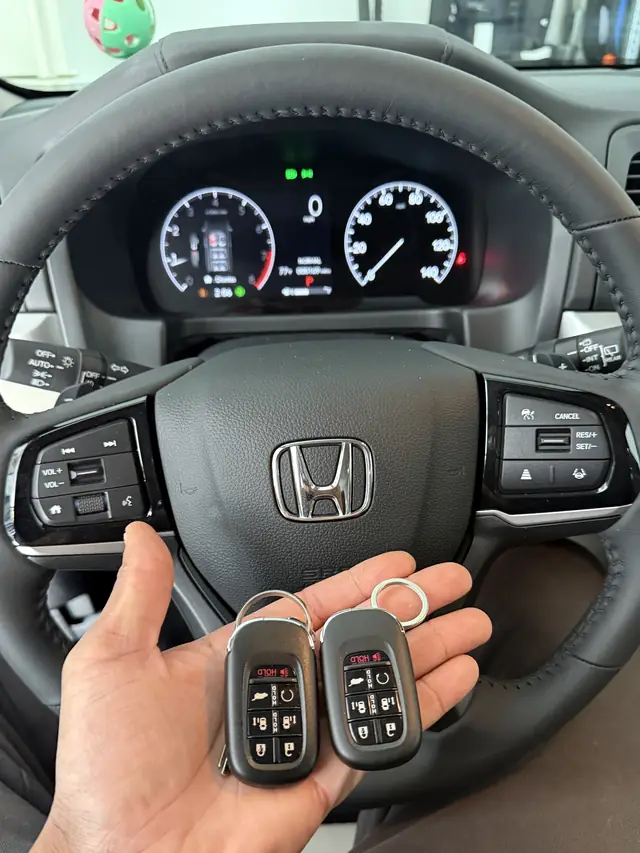 Two Honda smart keys held in front of a Honda steering wheel and instrument cluster