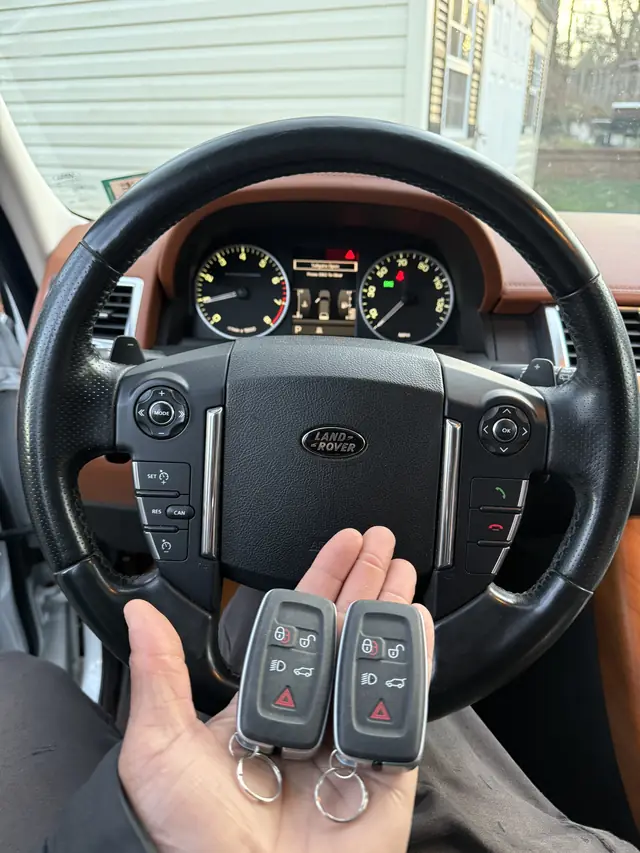 Two Land Rover smart keys held in front of a Range Rover Sport steering wheel