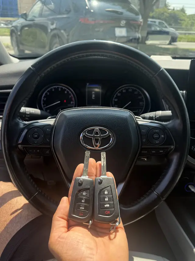 Two Toyota flip keys held in front of a Toyota steering wheel